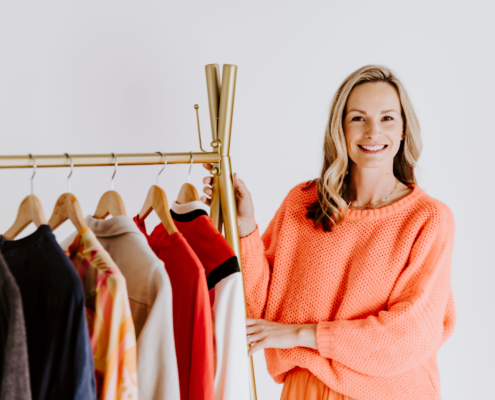 Kevin Ann Jordan standing next to a rack of clothes, showcasing a variety of stylish garments