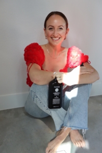 Amelia, wearing a red shirt, is holding an Oliveda product, smiling and showcasing the item.